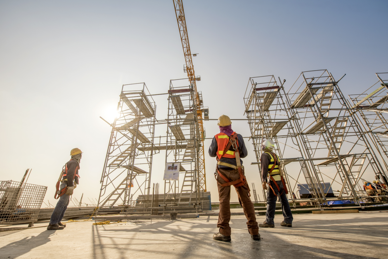 Construction engineers supervising progress of construction project stand on new concrete floor top roof and crane background